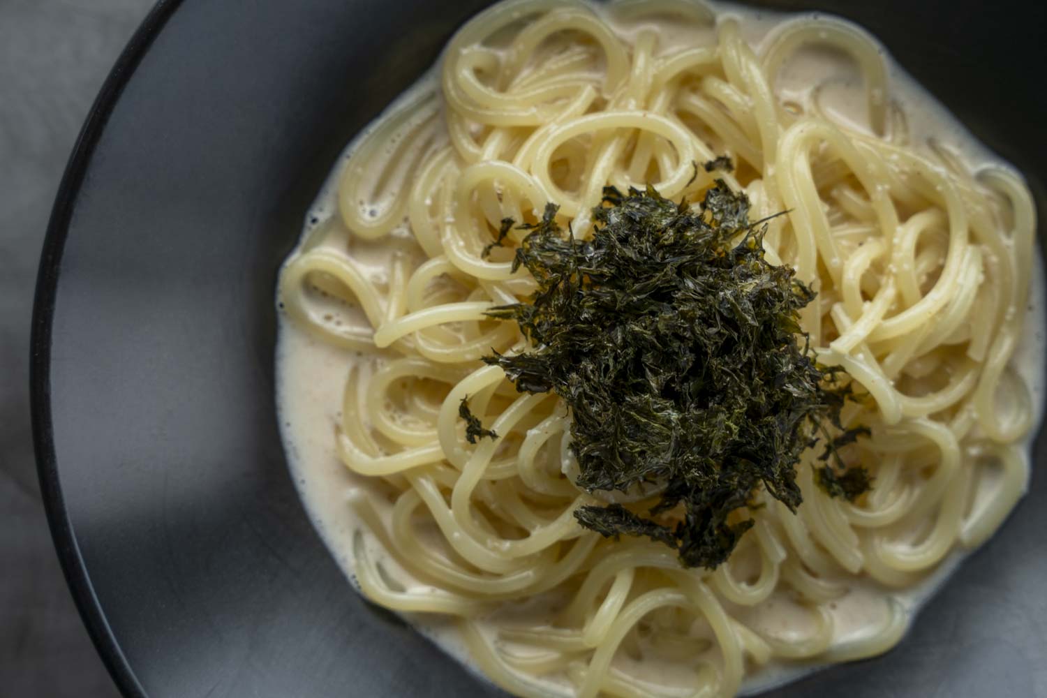 黒いボウルに盛られた明太子クリームパスタ、上に刻み海苔をトッピング