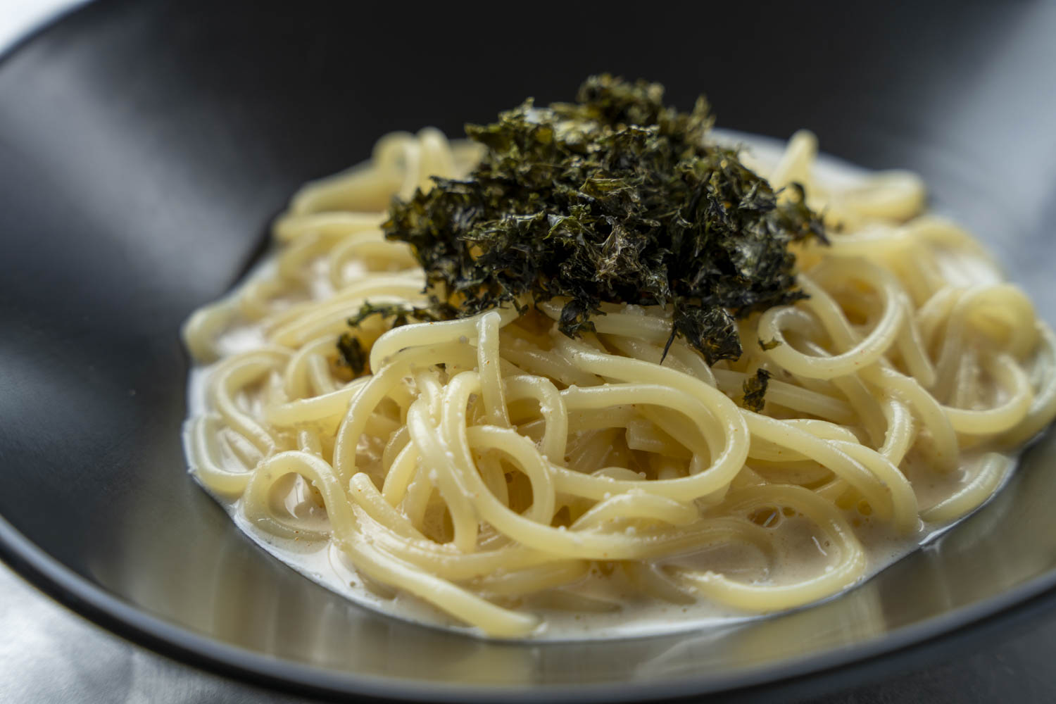 黒いボウルに盛られた明太子クリームパスタ、上に刻み海苔をトッピング