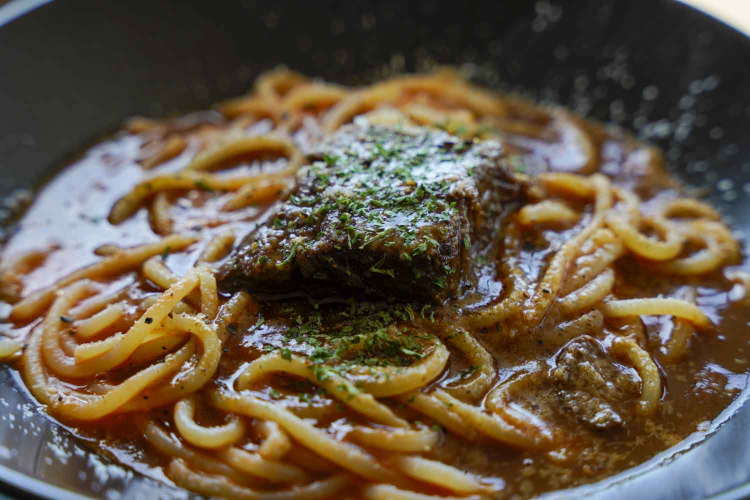 牛スネ肉のトロトロ煮を乗せた濃厚トマトソースパスタのアップ写真