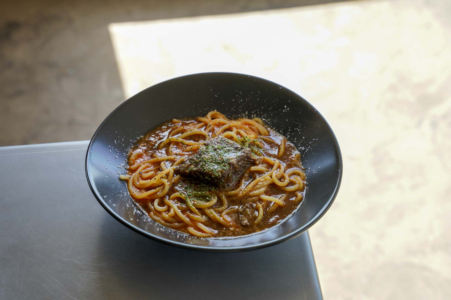 牛スネ肉のトロトロ煮を乗せた濃厚トマトソースパスタのアップ写真